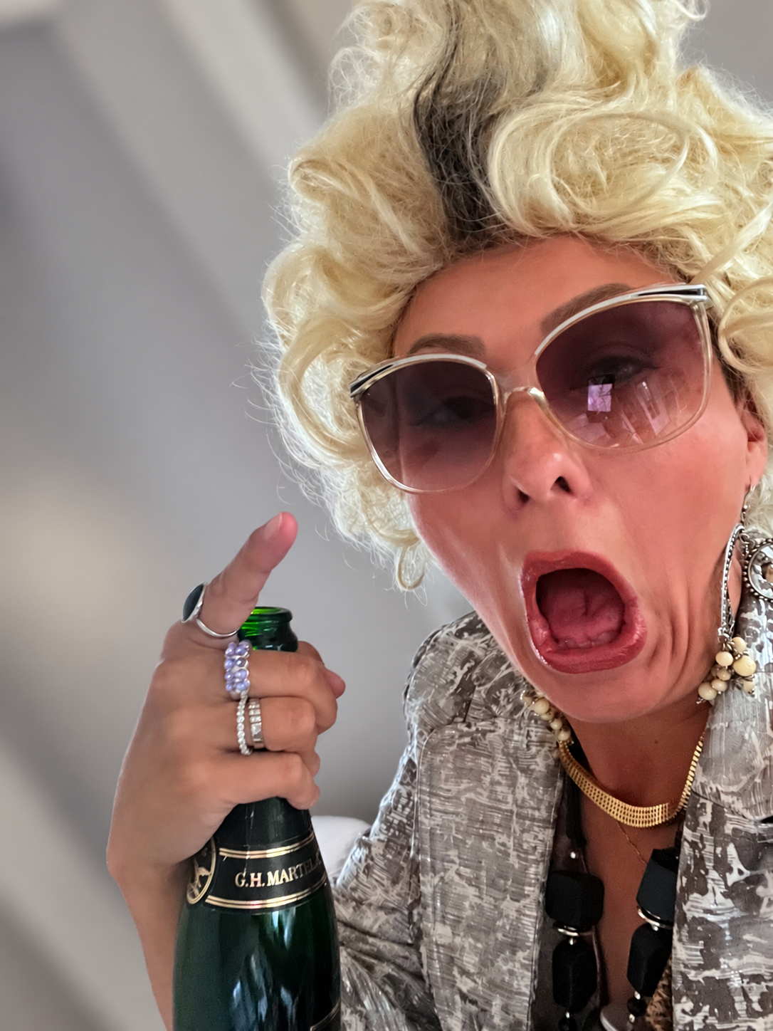 Laina Hefner -hahmo vaaleassa peruukissa ja aurinkolaseissa avaamassa kuohuviinipulloa